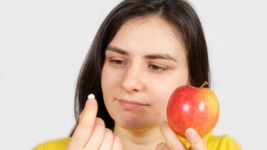 Pige med æble i den ene hånd kigger nysgerrigt på vitaminpille i den anden hånd