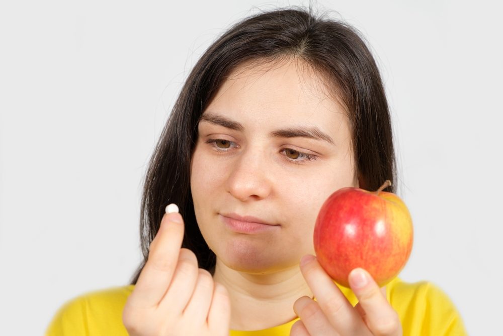 Pige med æble i den ene hånd kigger nysgerrigt på vitaminpille i den anden hånd