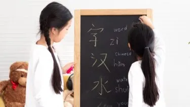 To piger, der skriver kinesiske tegn samt de tilhørende pinyin-udtaler og engelske oversættelser på en tavle.