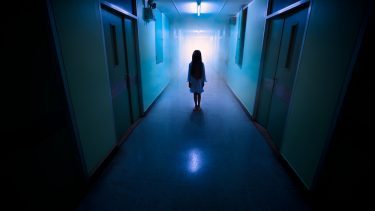 Mareridtsagtig scene, lille pige står alene i en lang, uhyggelig hospitalsgang