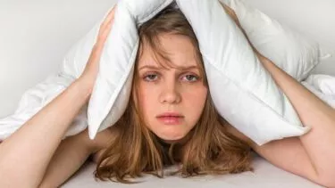Ung kvinde ser udkørt ud og holder sig for ørerne med sin hovedpude