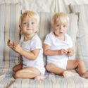 To hvidblonde rollinger på omkring et år sidder i en sofa og kigger på kameraet