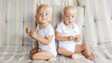 To hvidblonde rollinger på omkring et år sidder i en sofa og kigger på kameraet