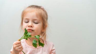 Et nærbillede af en lille pige der spiser koriander og ser utilfreds ud.