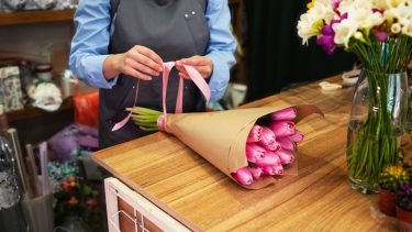 Blomsterhandlers hænder er i gang med at pakke en buket lyserøde tulipaner ind med en lyserød sløjfe om