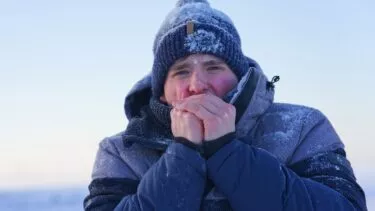 Mand med tophue og vinterjakke puster sig i hænderne på en kold dag med sne og is