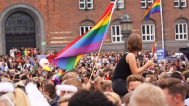En menneskemængde er samlet foran rådhuset i København. Regnbue-prideflag vejrer i vinden