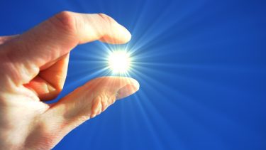 Hånd holdes op mod en blå himmel og laver en optisk illusion, hvor fingrene kniber sammen om Solen