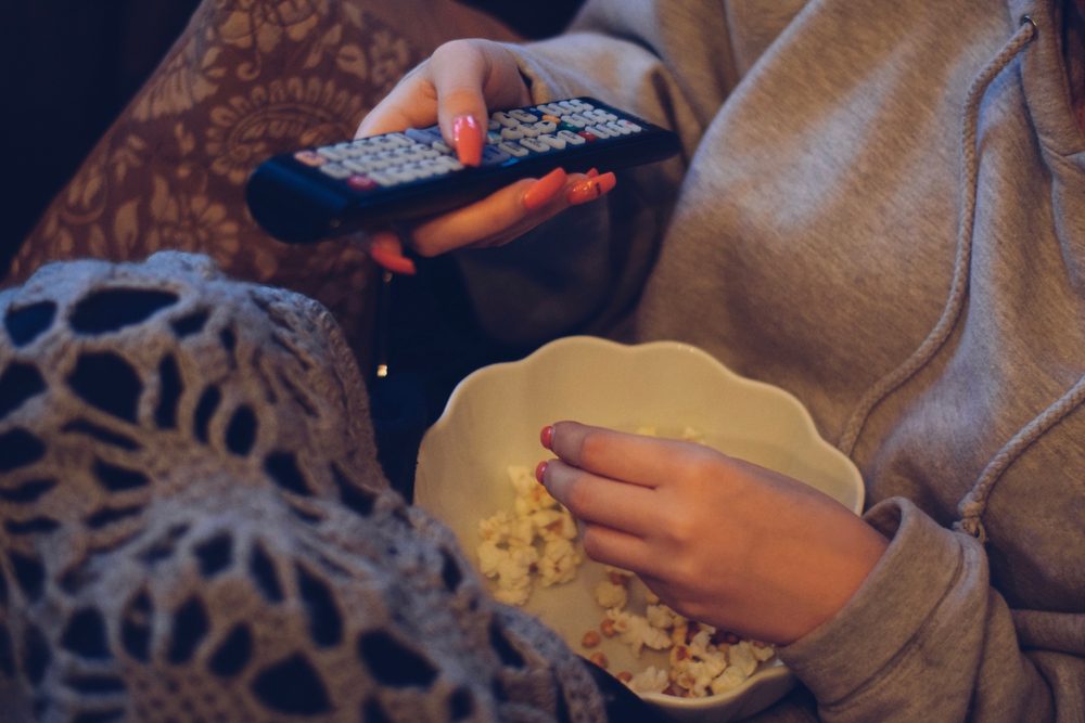Closeup af hænder, der spiser popcorn og holder på en fjernbetjening samtidig.