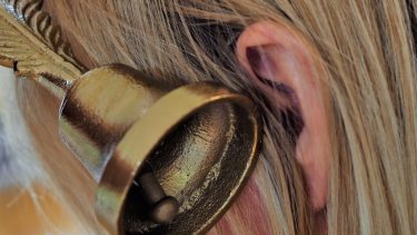 Tinnutus illustreret ved et nærbillede af en klokke sat op til øret på en person med blond hår