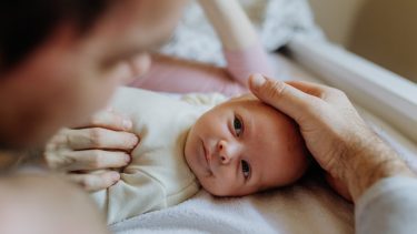 Baby på puslebord kigger op på forælderen