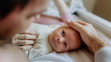 Baby på puslebord kigger op på forælderen