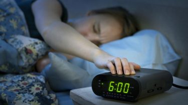 kvinde trykker pa snooze knap om morgenen