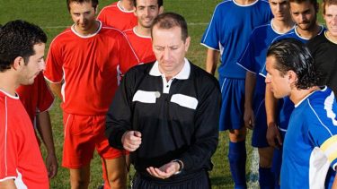 Fodbolddommer slår plat eller krone, mens holdene kigger på