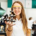 Ung pige i skolelokale holder model af molekyler op