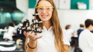Ung pige i skolelokale holder model af molekyler op