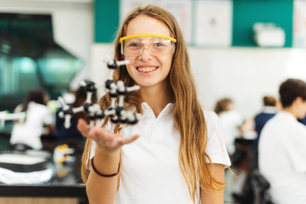 Ung pige i skolelokale holder model af molekyler op