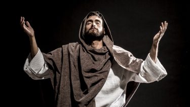'Jesus' sidder i skrædderstilling med løftede hænder og lukkede øjne