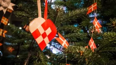 Dansk juletræ pyntet med et rødt og hvidt flettet hjerte og små danske flagguirlander mellem grønne fyrretræsgrene.