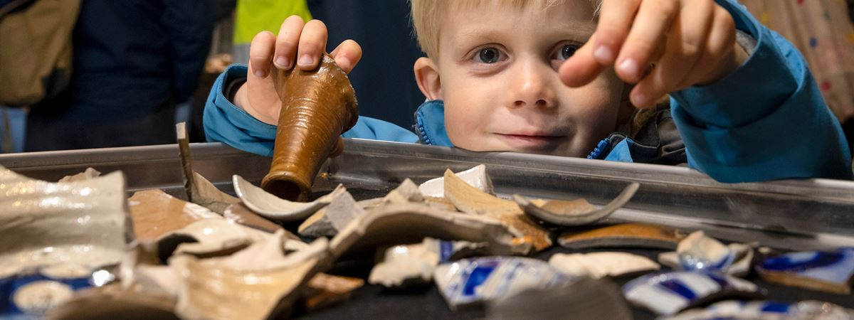 Lille dreng med et stort smil på læberne og potteskår fra Arkæologisk Værksted i hænderne.