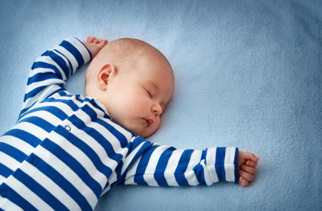 en baby med hvid- og blåstribet sparkedragt sover på et blåt lagen