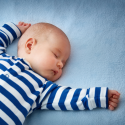 en baby med hvid- og blåstribet sparkedragt sover på et blåt lagen
