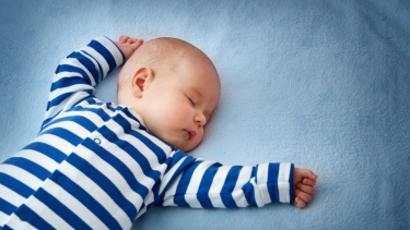 en baby med hvid- og blåstribet sparkedragt sover på et blåt lagen