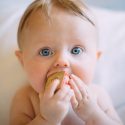 Baby med blå øjne og legetøj i munden kigger betuttet ind i kameraet