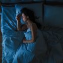 Kvinde der sover i blåt sengetøj i et dunkelt værelse med trægulve og en smule måneskin, der lyser rummet lidt op