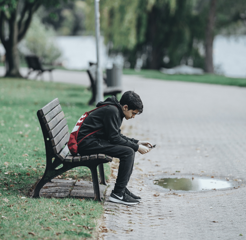 Teenage dreng, der sidder på en bænk med sin telefon