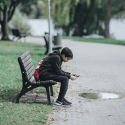 Teenage dreng, der sidder på en bænk med sin telefon