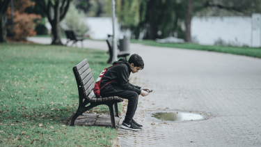 Teenage dreng, der sidder på en bænk med sin telefon