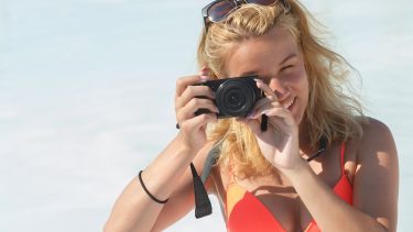 Pige på strand tager foto med digitalkamera