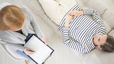 Kvinde ligger på sofa og bliver hypnotiseret af terapeut eller behandler