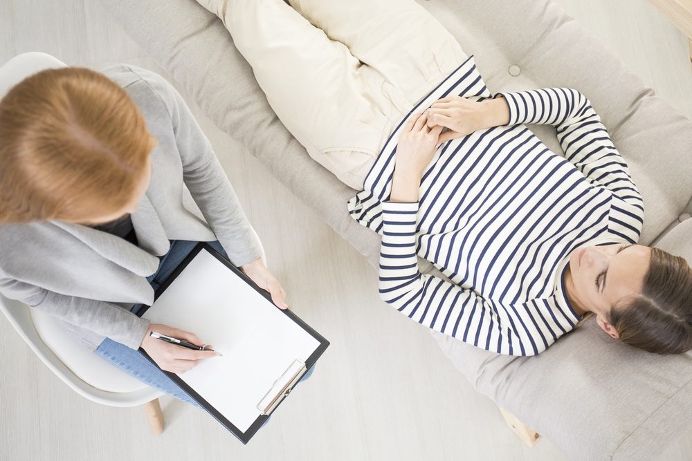Kvinde ligger på sofa og bliver hypnotiseret af terapeut eller behandler