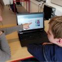Barn og voksen sidder foran en laptop og kigger på skærm med læseapp til ordblinde