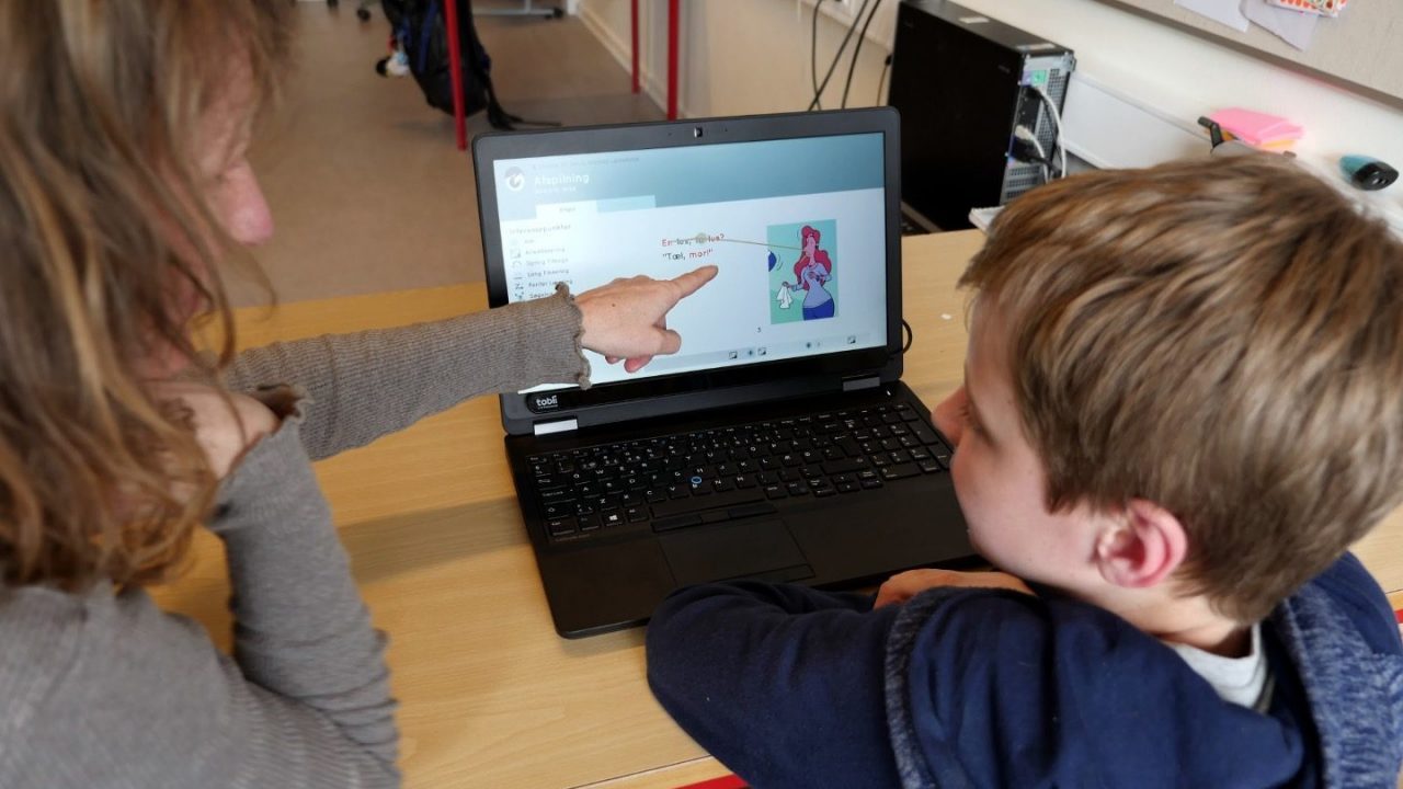 Barn og voksen sidder foran en laptop og kigger på skærm med læseapp til ordblinde