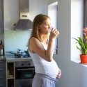 Lyshåret ung kvinde står i et køkken og drikker et glas postevand