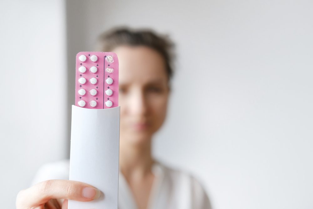 Ung kvinde holder en lyserød pakke med p-piller op, kvinden er sløret, pillerne er i fokus