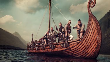 Foto af vikingeskib med vikinger ombord mod en truende aftensky
