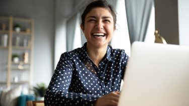 Storsmilende kvinde foran computer på arbejdspladsen