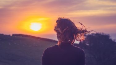Kvinde med ryggen til ser på smuk sommer-solnedgang