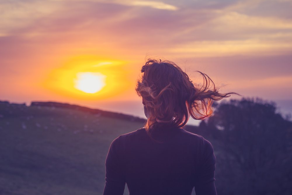 Kvinde med ryggen til ser på smuk sommer-solnedgang