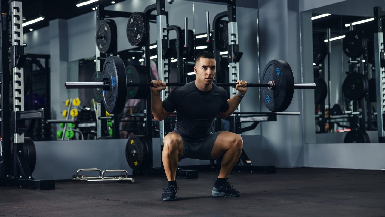 Mand træner squats med vægtstang i fitnesscenter