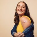 Smilende ung kvinde med plaster på overarmen efter vaccine