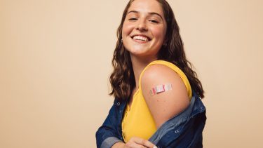 Smilende ung kvinde med plaster på overarmen efter vaccine