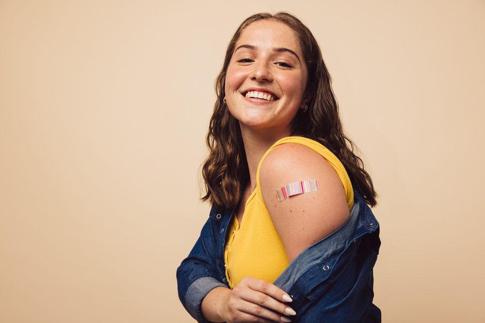 Smilende ung kvinde med plaster på overarmen efter vaccine