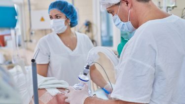 Anæstesilæge bedøver patient, i baggrunden står en sygeplejerske med blåt hårnet