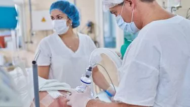 Anæstesilæge bedøver patient, i baggrunden står en sygeplejerske med blåt hårnet