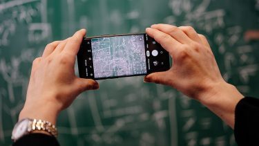 Mand fotograferer tavle med sin mobiltelefon. Der er kompliceret algebra skrevet op på tavlen.